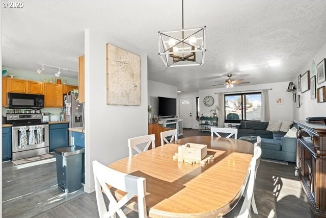 dining space with dark wood-type flooring, track lighting, ceiling fan with notable chandelier, and a textured ceiling