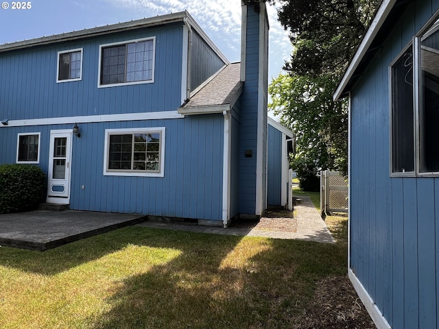 1011 Heather Ct, Reedsport, OR 97467 - rear view of house with a chimney, a lawn, a shingled roof, and a patio