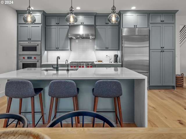 kitchen featuring built in refrigerator, a kitchen island with sink, and range hood