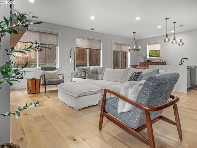 living room with an inviting chandelier, sink, and light hardwood / wood-style floors