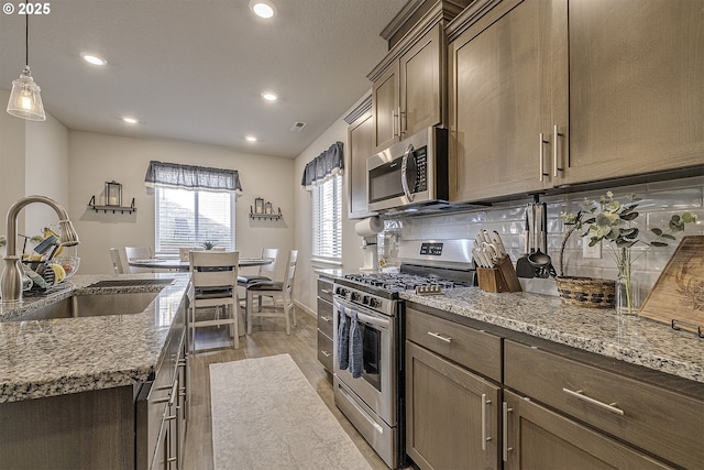 kitchen featuring appliances with stainless steel finishes, hanging light fixtures, light stone countertops, light hardwood / wood-style flooring, and sink