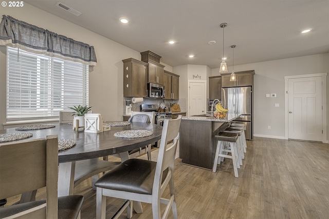 kitchen featuring light stone countertops, appliances with stainless steel finishes, decorative light fixtures, tasteful backsplash, and light hardwood / wood-style floors