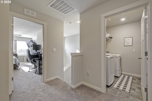 clothes washing area with a textured ceiling, light colored carpet, and washer and clothes dryer