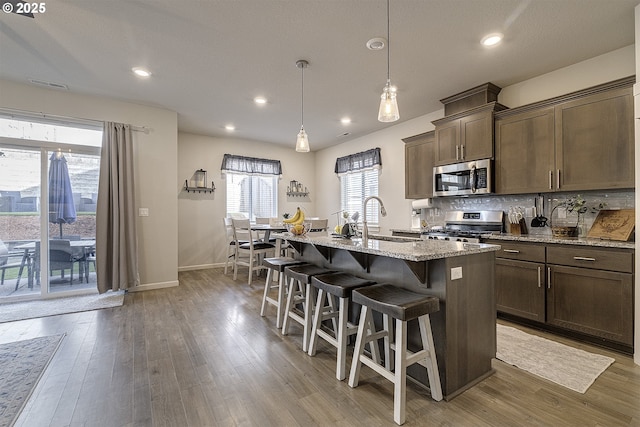 kitchen featuring appliances with stainless steel finishes, decorative light fixtures, sink, light stone counters, and a center island with sink