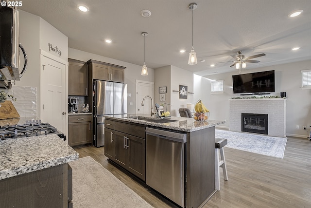 kitchen with appliances with stainless steel finishes, light hardwood / wood-style flooring, hanging light fixtures, light stone counters, and a center island with sink