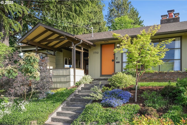 doorway to property featuring a chimney and a shingled roof