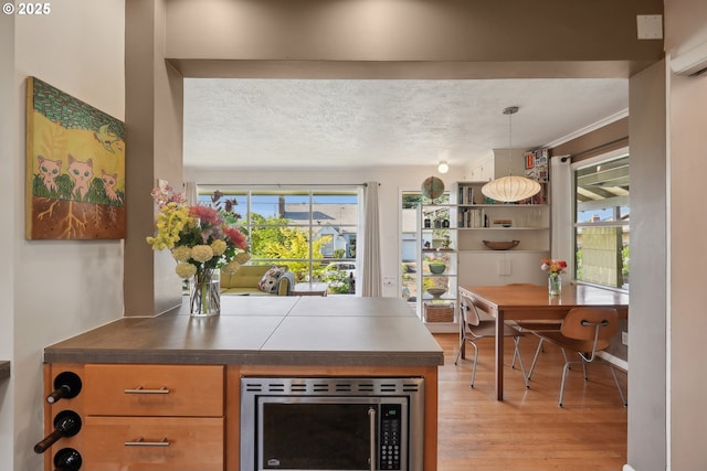 bar area featuring stainless steel microwave, a wall mounted AC, light wood-style floors, hanging light fixtures, and a textured ceiling