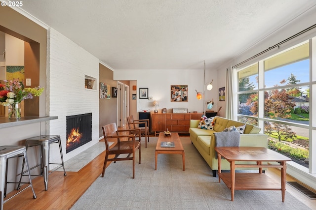 living area with a brick fireplace, a textured ceiling, light wood-type flooring, and ornamental molding