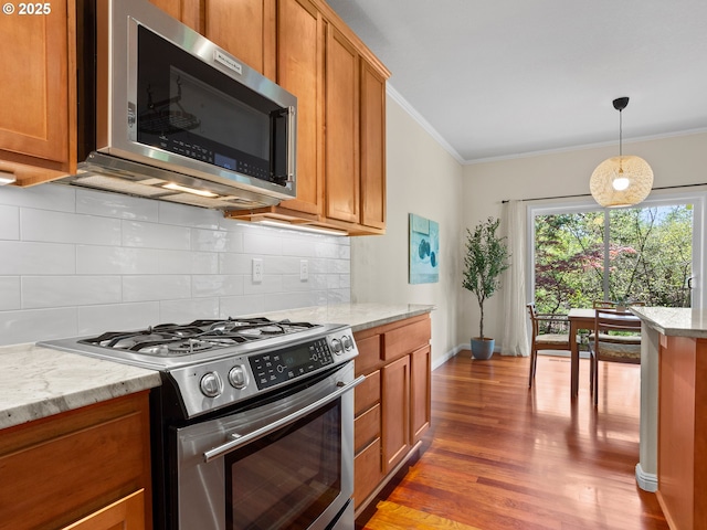 kitchen with ornamental molding, appliances with stainless steel finishes, light wood finished floors, brown cabinets, and decorative backsplash