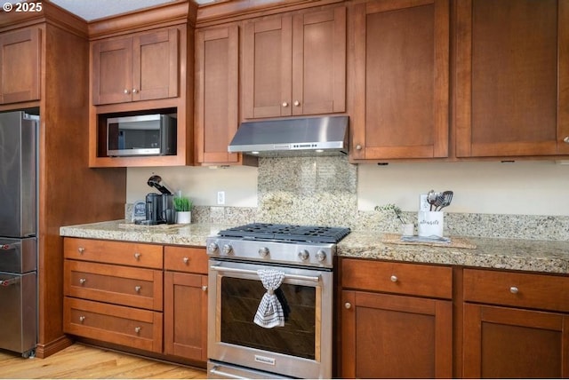 kitchen featuring under cabinet range hood, brown cabinets, appliances with stainless steel finishes, and light wood-type flooring