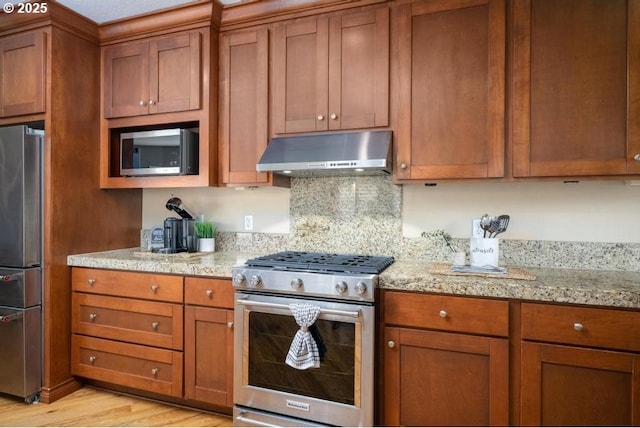 kitchen featuring stainless steel appliances, under cabinet range hood, brown cabinets, and light wood-style flooring