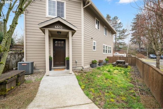 view of exterior entry with cooling unit, a yard, and fence