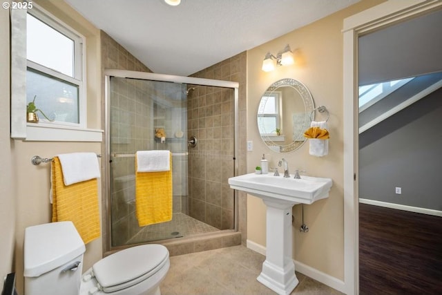 bathroom with toilet, a stall shower, plenty of natural light, and baseboards