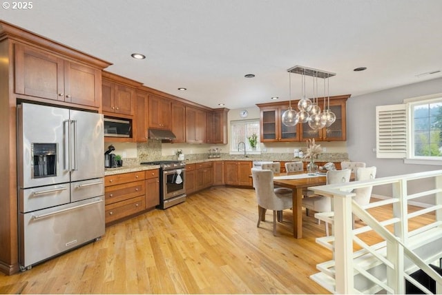 kitchen featuring stainless steel appliances, light wood finished floors, brown cabinetry, hanging light fixtures, and a sink