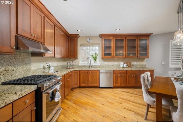 kitchen with brown cabinets, under cabinet range hood, a sink, stainless steel appliances, and light wood finished floors