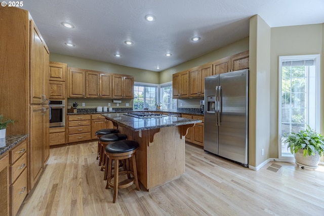 kitchen featuring stainless steel appliances, light wood-style floors, a breakfast bar, brown cabinets, and dark stone countertops