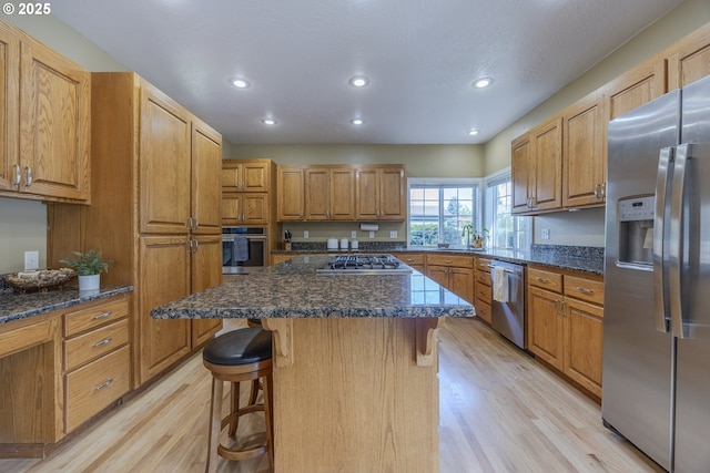 kitchen with appliances with stainless steel finishes, light wood-style floors, a kitchen breakfast bar, recessed lighting, and dark stone counters