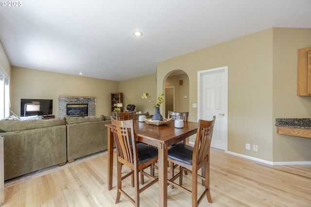 dining room with arched walkways, light wood finished floors, a glass covered fireplace, baseboards, and recessed lighting