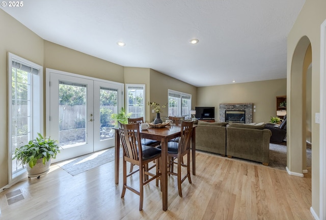 dining space with light wood-style flooring, french doors, a glass covered fireplace, arched walkways, and recessed lighting