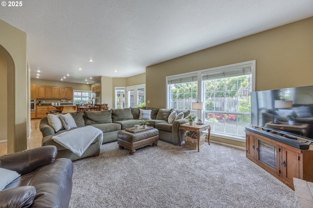living area featuring arched walkways, recessed lighting, and light colored carpet