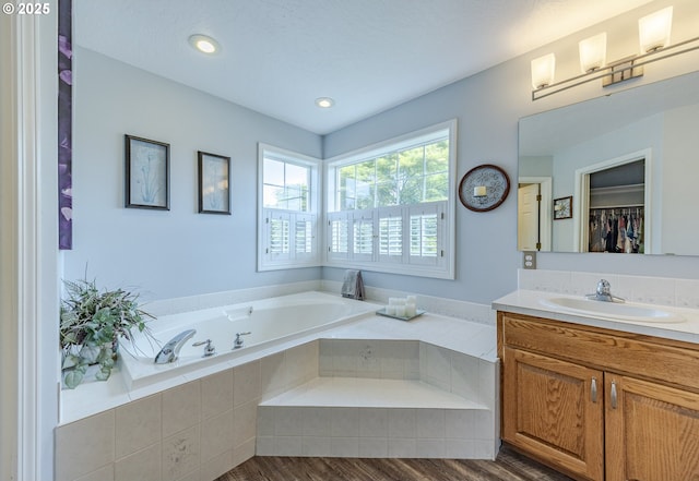 bathroom with a bath, vanity, a spacious closet, recessed lighting, and wood finished floors