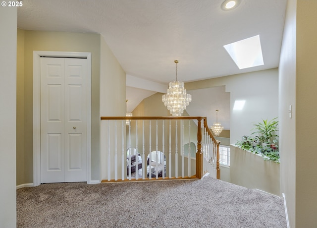 hall featuring a chandelier, carpet, a skylight, an upstairs landing, and baseboards
