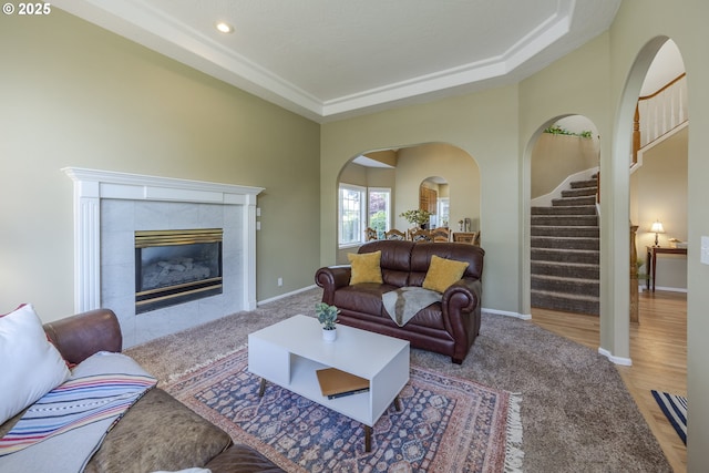 carpeted living area with stairs, baseboards, a tiled fireplace, arched walkways, and recessed lighting