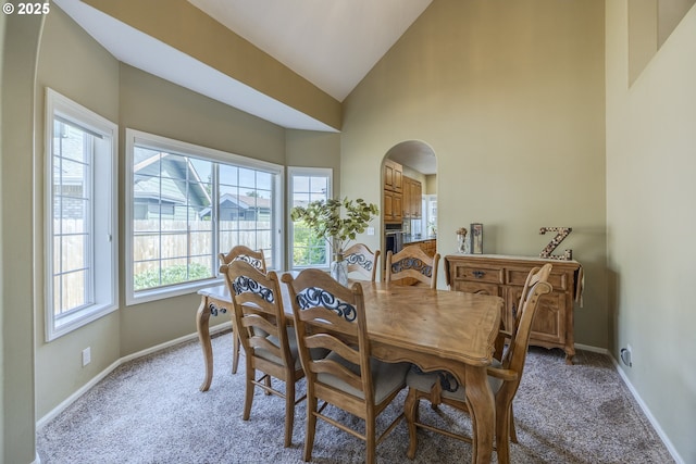 dining space featuring light carpet, plenty of natural light, arched walkways, baseboards, and high vaulted ceiling