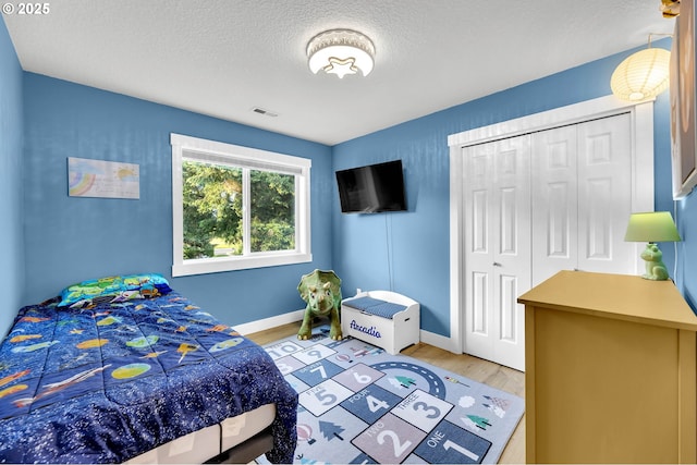 bedroom featuring a textured ceiling, visible vents, baseboards, a closet, and light wood finished floors