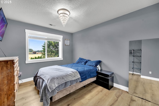 bedroom with visible vents, baseboards, light wood-type flooring, a textured ceiling, and a notable chandelier