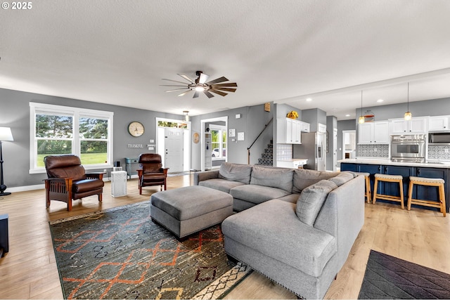 living room featuring light wood-style floors, baseboards, a ceiling fan, and stairs