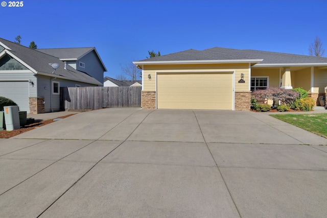 view of front facade featuring an attached garage, stone siding, driveway, and fence