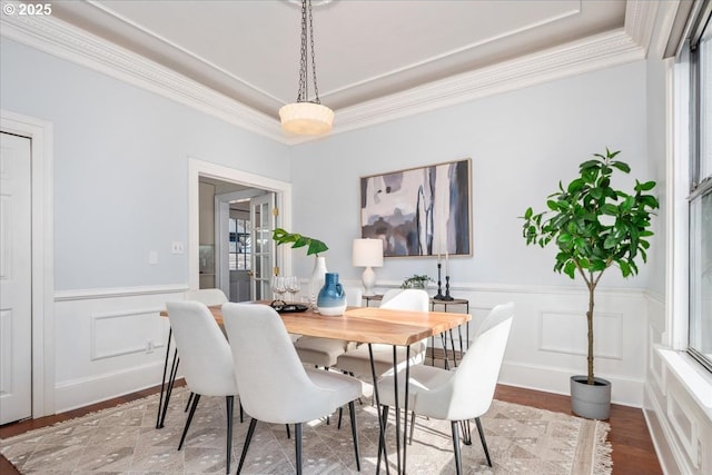 dining room with a wainscoted wall, wood finished floors, crown molding, and a decorative wall