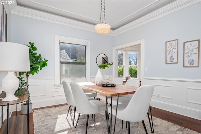 dining space featuring a decorative wall, wainscoting, wood finished floors, and ornamental molding