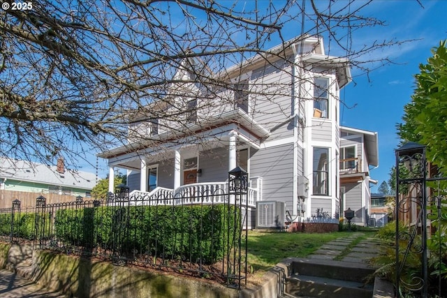 view of home's exterior with a porch, central AC unit, and a fenced front yard