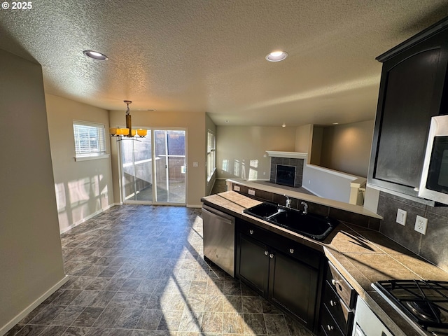 kitchen with decorative light fixtures, stainless steel appliances, decorative backsplash, a sink, and dark cabinetry