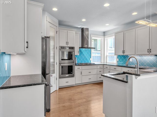 14509 SE Faircrest St, Clackamas, OR 97015 - kitchen with wall chimney range hood, appliances with stainless steel finishes, backsplash, light wood finished floors, and recessed lighting