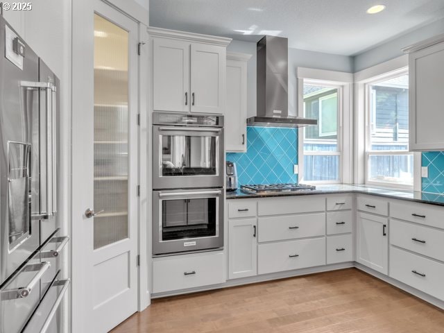 14509 SE Faircrest St, Clackamas, OR 97015 - kitchen featuring stainless steel appliances, wall chimney range hood, tasteful backsplash, light wood-style floors, and white cabinetry