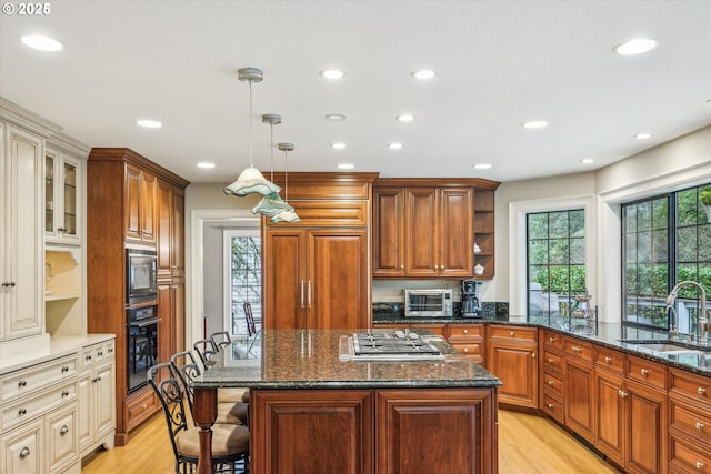 kitchen featuring stainless steel gas stovetop, light hardwood / wood-style floors, black oven, and sink