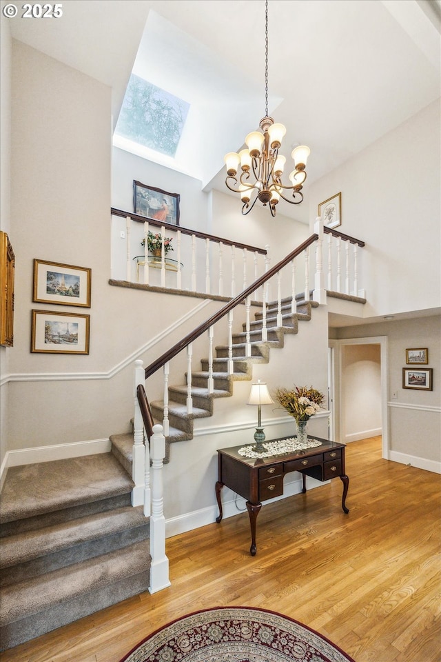 stairs featuring a skylight, a towering ceiling, a chandelier, and hardwood / wood-style flooring