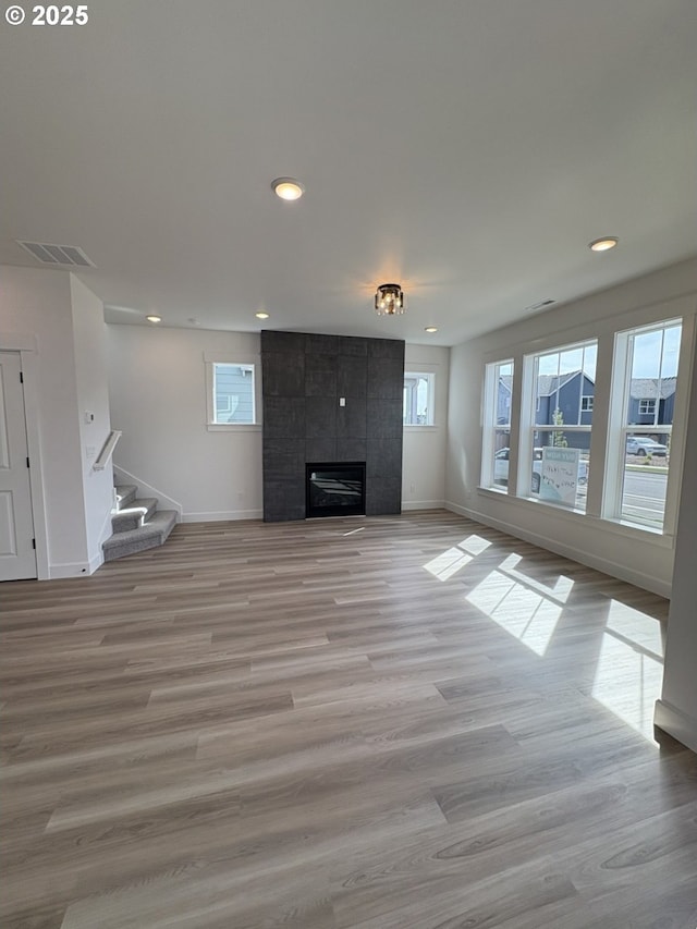 unfurnished living room featuring a wealth of natural light, visible vents, stairs, and baseboards