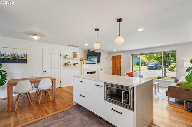 kitchen featuring visible vents, a lit fireplace, recessed lighting, white cabinetry, and stainless steel microwave
