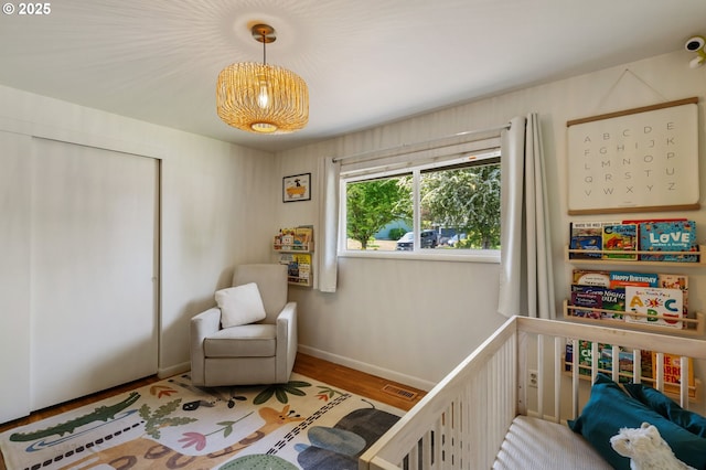 bedroom featuring visible vents, a closet, wood finished floors, baseboards, and a nursery area
