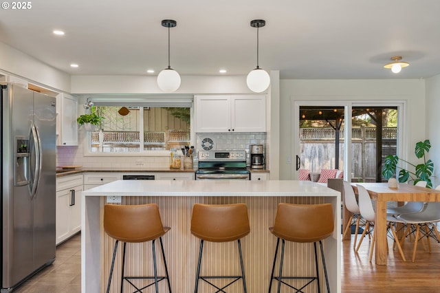 kitchen featuring stainless steel appliances, a breakfast bar, white cabinetry, and tasteful backsplash