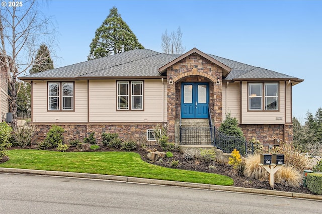 view of front facade with central AC, a shingled roof, stone siding, and a front yard