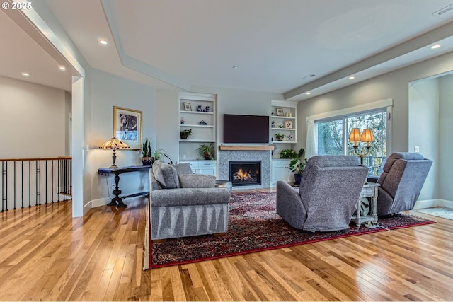 living area with baseboards, visible vents, built in features, a lit fireplace, and hardwood / wood-style floors