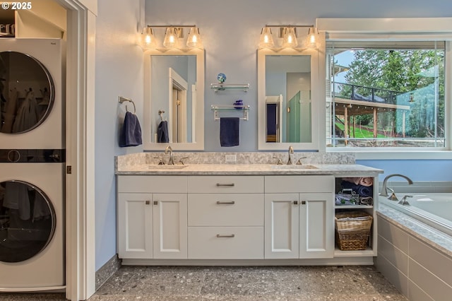 full bath featuring stacked washer and dryer, a tub to relax in, double vanity, and a sink