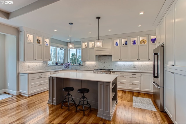 kitchen with appliances with stainless steel finishes, light countertops, a center island, white cabinets, and light wood-style floors
