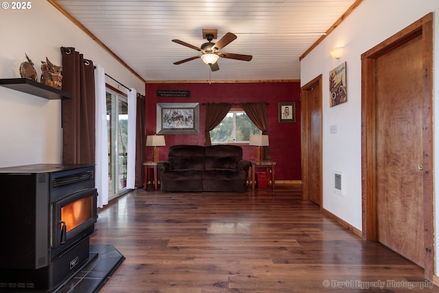 living room featuring dark wood-type flooring, a wood stove, crown molding, and ceiling fan