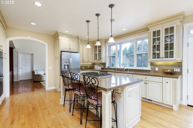 kitchen featuring arched walkways, a breakfast bar area, appliances with stainless steel finishes, tasteful backsplash, and dark stone countertops